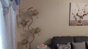 Un salon avec un canapé gris foncé, des coussins à motifs, un tableau abstrait accroché au mur et une plante décorative en métal.