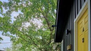 Eine Holzterrasse mit einer gelben Tür, einem kleinen Tisch mit Stühlen und einem Baum im Hintergrund.
