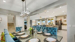 A modern dining area with a long table set for six, surrounded by blue upholstered chairs. - Coachella Escape. Brand New Luxury home in gated community. (Indio)
