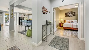 A modern hotel room with a bed, bedside table, and lamp. There is a dining area with a table and chairs. The room has a large window and a view of the outside. - Coachella Escape. Brand New Luxury home in gated community. (Indio)