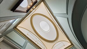 Un plafond richement décoré, orné de motifs dorés et surmonté d’un luminaire circulaire central.