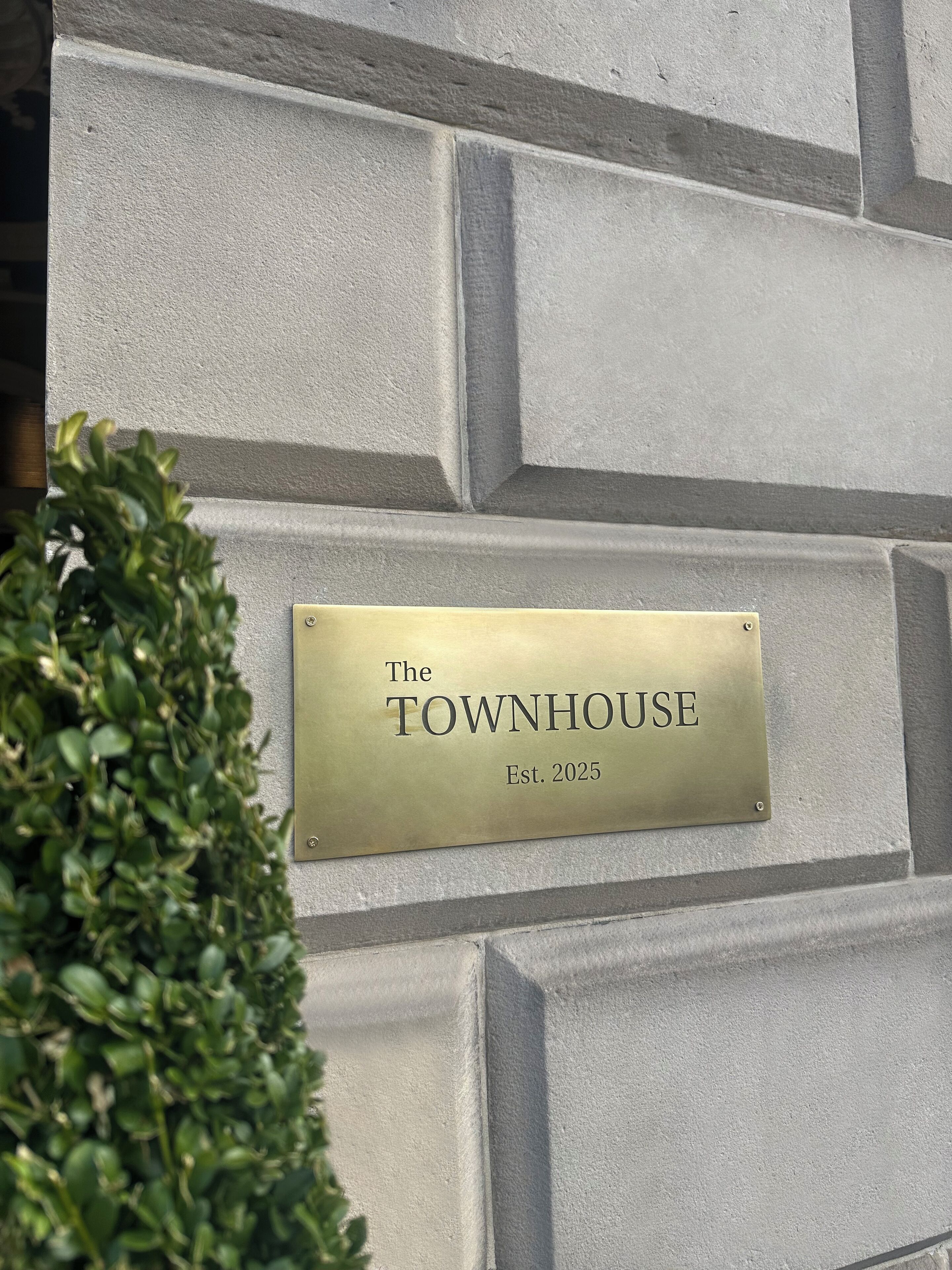 Una placa en una paret amb textura que mostra el text "The TOWNHOUSE Est. 2025".