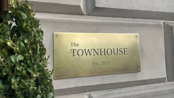Una placa en una paret amb textura que mostra el text "The TOWNHOUSE Est. 2025".