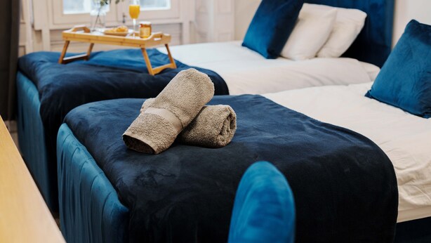 A hotel room with two beds, each with a dark blue bedspread and a beige towel on one bed. There is a wooden tray with breakfast items on the window sill. - 30% OFF Monthly | Family & Work Stays - Contact us for better rates! (Woodhouse)