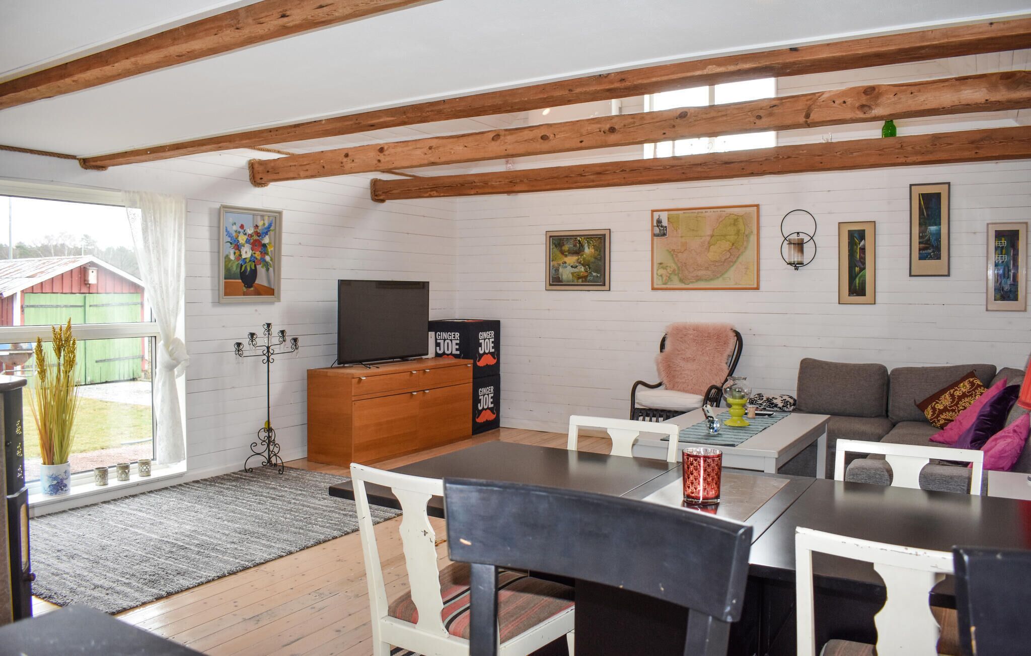 A cozy living room with a wooden ceiling, a television on a wooden cabinet, a dining table with chairs, and a sofa.