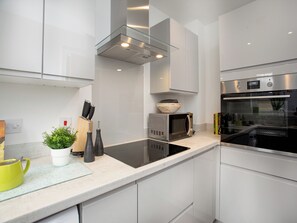 A modern kitchen with white cabinets, a black stove, a microwave, and a glass shelf.