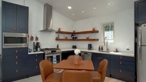 Una cocina moderna con armarios oscuros, un microondas de acero inoxidable, una estufa a gas y una mesa de comedor con sillas.
