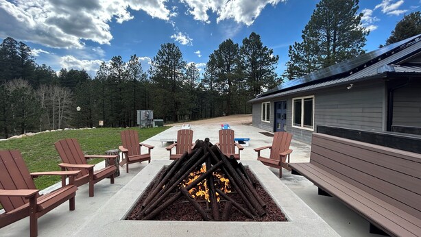 Un patio con sillas Adirondack, un brasero y un edificio con ventanas grandes.