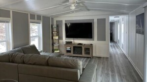Un salón amplio con un televisor de pantalla plana grande, un ventilador de techo y un mueble empotrado para entretenimiento.