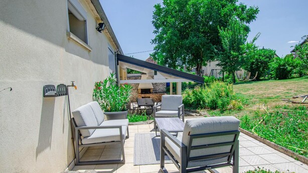 Une terrasse extérieure avec deux chaises blanches dotées de coussins, une petite table et un espace barbecue.