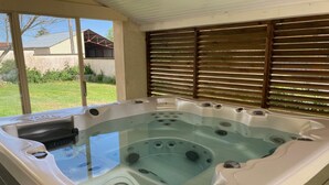 Un bain à remous doté d’une enceinte en verre, d’une terrasse en bois et offrant une vue sur une maison et la verdure environnante.