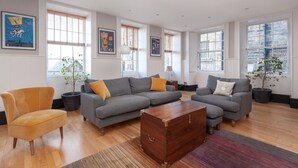 A spacious living room with a grey sectional sofa, a wooden chest of drawers, and a yellow armchair.