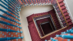 A spiral staircase with blue balusters and red patterned carpet.