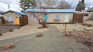 A gravel driveway leading to a house with a blue roof and a yellow door. - Mama Bear’s Den- Pet Friendly (Burns)