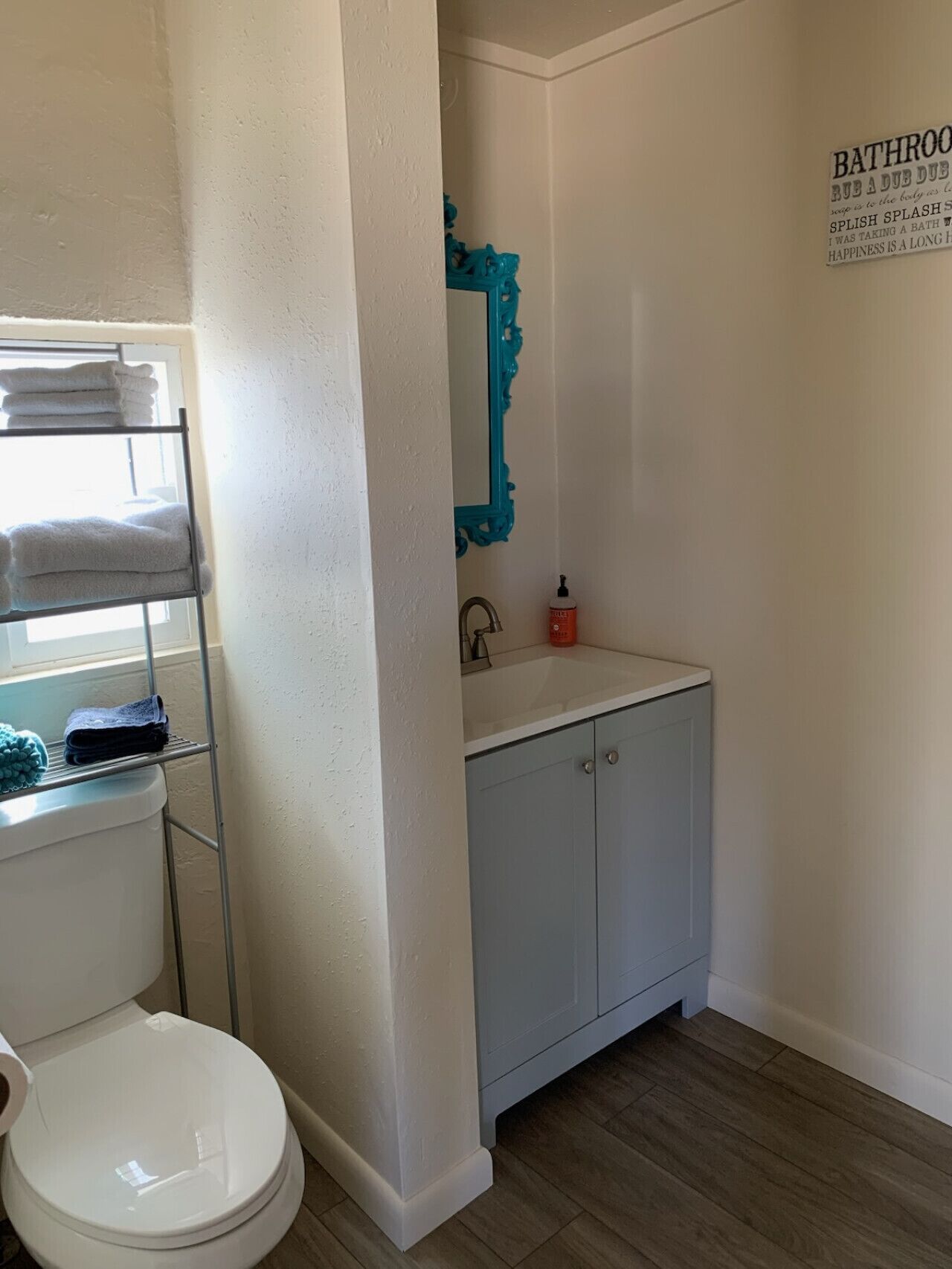 A bathroom with a white toilet, a blue vanity with a mirror, and a shelf with towels.