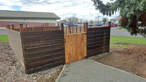 A wooden gate with a metal handle, leading to a gravel path and a paved road. - Mama Bear’s Den- Pet Friendly (Burns)
