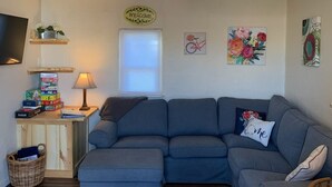 A living room with a sectional sofa, a TV mounted on the wall, a lamp, and artwork. - Mama Bear’s Den- Pet Friendly (Burns)