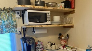 A compact kitchen with a microwave, coffee maker, and various kitchen utensils on shelves. - Mama Bear’s Den- Pet Friendly (Burns)