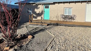 A house with a turquoise door, a patio with chairs, and a gravel driveway. - Mama Bear’s Den- Pet Friendly (Burns)