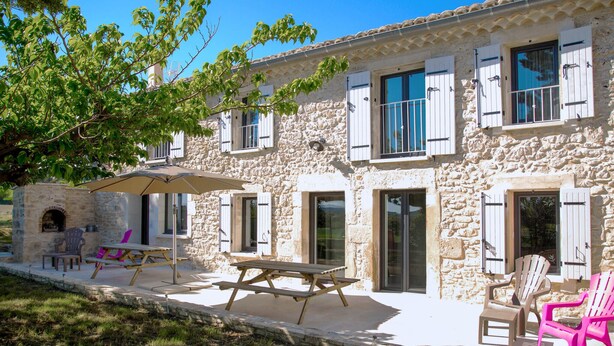 A stone building with white shutters, a patio with a table and chairs, and a tree providing shade. - Nice home in La Garde Adhémar (La Garde Adhémar)