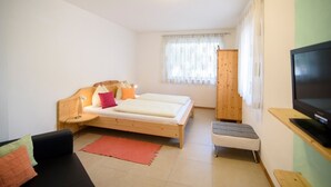 A bedroom with a bed, a TV, a small stool, a nightstand, and a window with curtains.