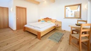 A bedroom with a wooden bed, a bedside table, a chair, a window, and a mirror.