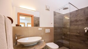 A modern bathroom with a large oval sink, a toilet, and a glass-enclosed shower.