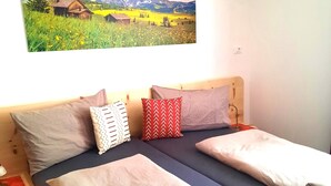 Ein Doppelbett mit Kopfstütze, zwei Kissen, ein Nachttisch mit Lampe sowie ein Wandbild mit Landschaftsmotiv.