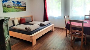 Ein Zimmer mit einem hölzernen Bett, einem Esstisch mit Stühlen, einem Bild an der Wand und einem Fenster mit Vorhängen.