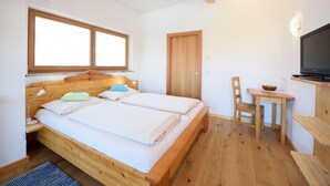 Une chambre à coucher avec un lit en bois, une petite table, une chaise, un téléviseur et une fenêtre.
