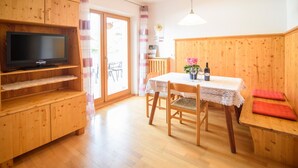A wooden interior with a TV on a shelf, a dining table with chairs, and a bench.