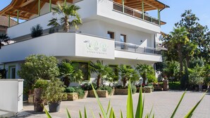 A multi-story building with a balcony, surrounded by potted plants and trees.