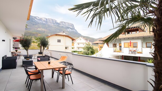 A balcony with a table and chairs, overlooking a mountainous landscape.