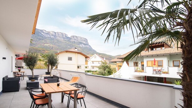A balcony with a table and chairs, potted plants, and a view of buildings and mountains.