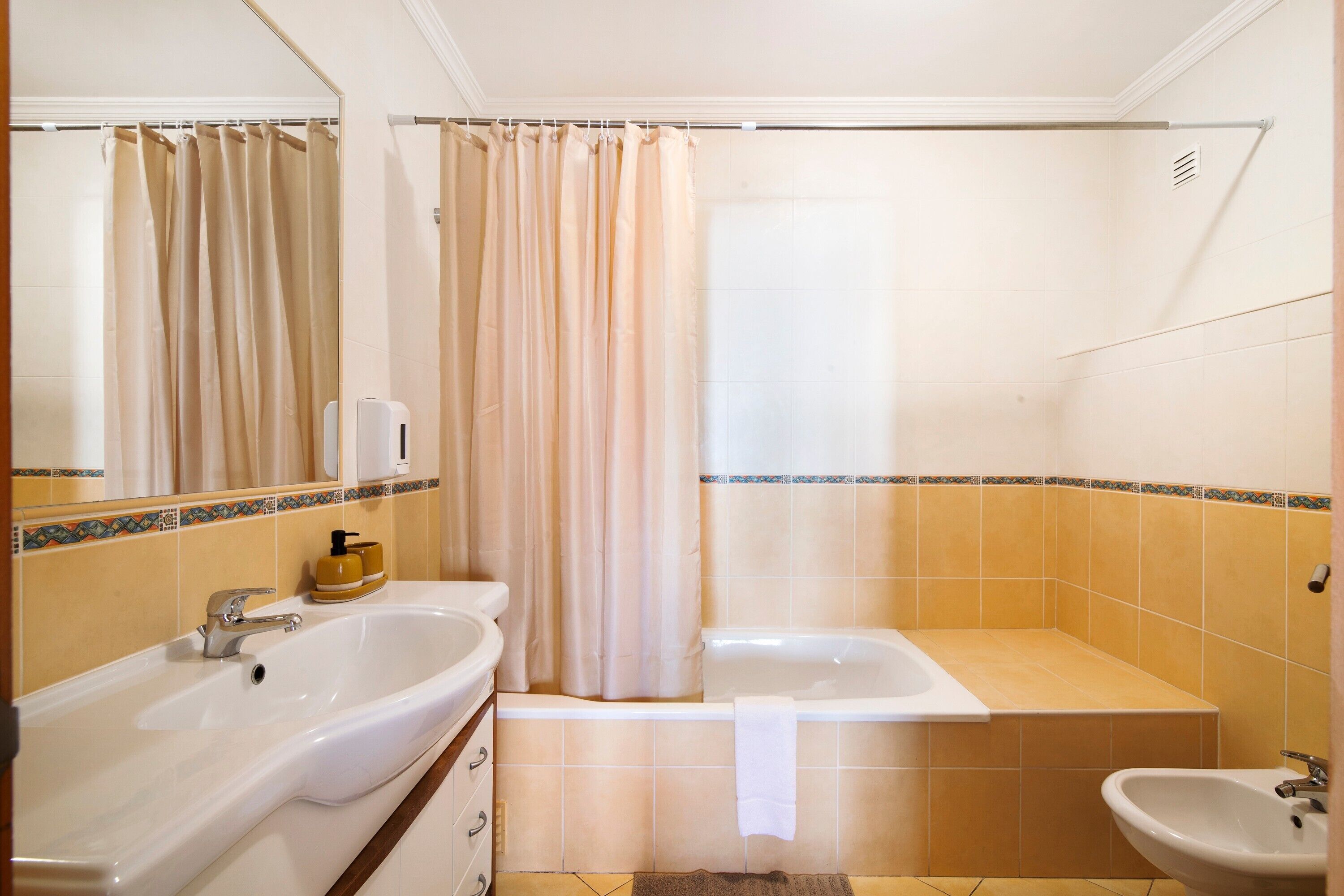 A bathroom with a sink, bathtub, shower curtain, and a bidet.