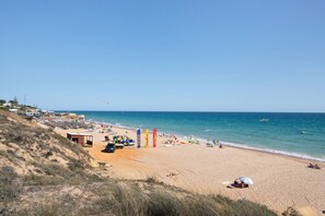 Une plage avec un rivage sablonneux, quelques parasols et un ciel dégagé.