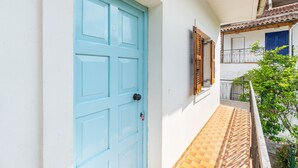 Una porta blava, un petit balcó amb un paviment de rajoles i una paret blanca amb una finestra i una porta.