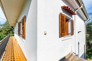 Un bâtiment blanc avec des volets en bois, un balcon doté d’un sol carrelé et une rambarde en métal.