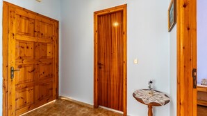 Un passadís amb dues portes de fusta, una taula petita amb cambrera de xarxa i un llum al sostre.