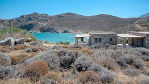 A coastal landscape with a stone building, rocky terrain, and a clear blue sea.