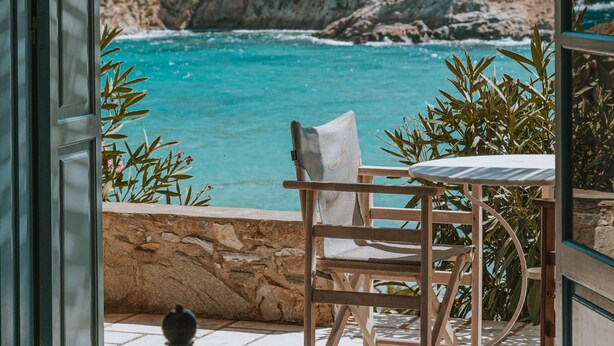 A room with a view of a coastal landscape, a table, and a chair.