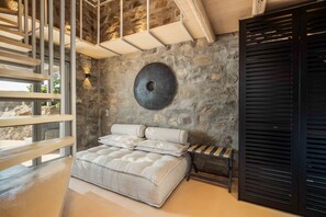 A modern bedroom with a stone wall, a round wall-mounted light, a bed with a headboard, and a wooden staircase.