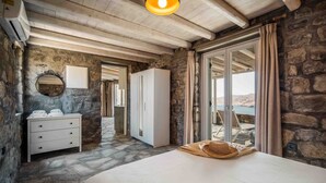 A bedroom with stone walls, a wooden ceiling, a bed, a wardrobe, a mirror, and a view of the outdoors. - Villa 'Vagia' with Private Pool, Private Terrace and Air Conditioning (S???f??)