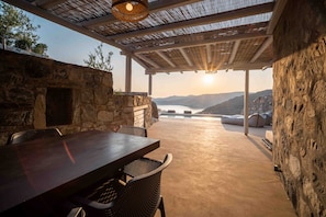 A covered outdoor dining area with a stone wall, a table, and chairs.