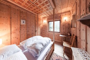 Una habitación de cabaña de madera con una cama, una silla, una mesa y un ventanal.