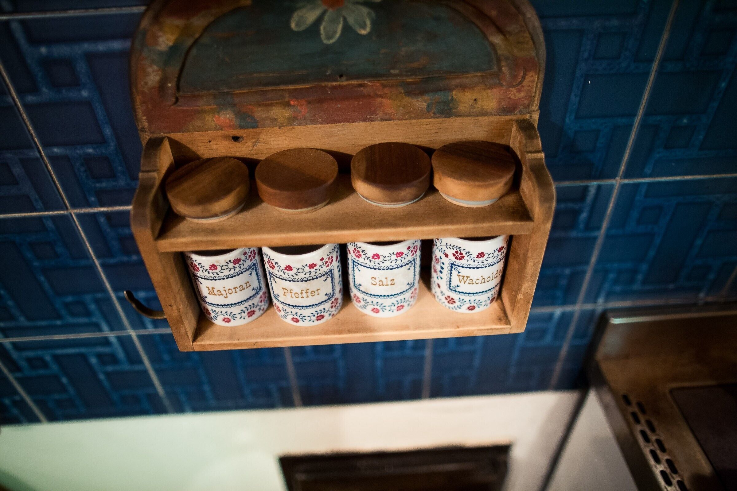 A wooden spice rack with five containers labeled 'Majora,' 'Pfeffer,' 'Salz,' and 'Wacholder.'
