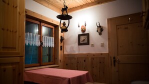 A room with wooden walls, a table with a red tablecloth, a hanging light fixture, and a door. - Chalet 'Am Reschensee' with Lake View, Private Terrace and Private Garden (Resia)