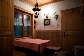 Ein Zimmer mit Holzwänden, einem Tisch mit roter Tischdecke, einer Pendelleuchte und einer Tür.