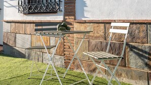 A patio with a table and chairs, a window with a metal grill, and a stone wall. - "La Azomadilla" Apartment with Shared Terrace and Wi-Fi (Totalán)