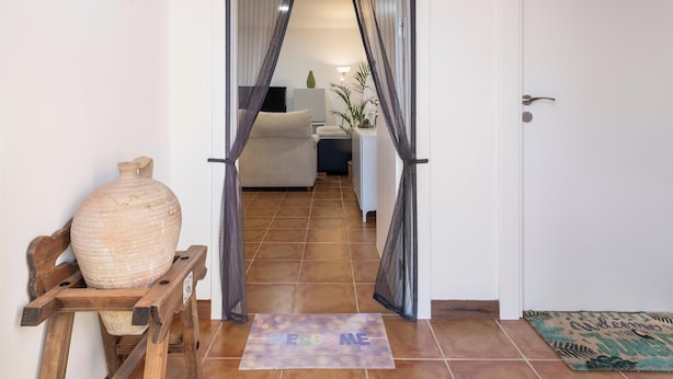 A hallway with a door marked '2', a welcome mat, a wooden stand with a vase, and a glimpse into a living area with a sofa and a plant. - "La Azomadilla" Apartment with Shared Terrace and Wi-Fi (Totalán)